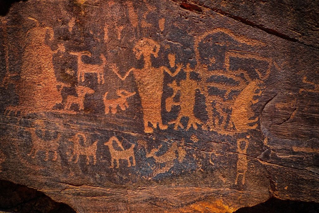 Image Description: Orange human and animal like petroglyphs on a dark background.